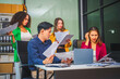 © Phushutter - Asian colleagues, middle-aged man and young woman, happily collaborate in office workplace. They gather around laptop, discussing project management, startup plans, teamwork paper stacks on desk.
