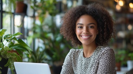 Wall Mural - A woman with curly hair is smiling and sitting at a table with a laptop. She is happy and relaxed