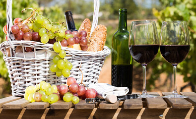 Still life with glass of red wine grapes and picnic basket on table