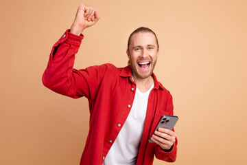 Canvas Print - Photo of nice young man raise fist hold phone wear red shirt isolated on beige color background