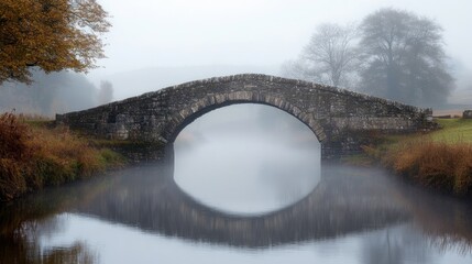 A historic stone bridge arching over a misty river in a peaceful countryside.