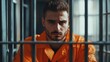 © Yeivaz - Thoughtful prisoner in an orange prison uniform gazes intently through cold metal bars of dim cell