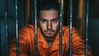 © Yeivaz - Thoughtful prisoner in an orange prison uniform gazes intently through cold metal bars of dim cell