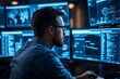 © nurionstudio - A man in a dark room looks at computer screens with blue lights reflecting on his face.