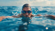© mahamad - Man swimming crawl stroke in the blue ocean open water. Portrait of an athletic young male triathlete swimming crawl, wearing a cap and swimming goggles, training for a triathlon.