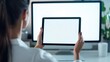 © DREAMERLYN STUDIO - A tech-savvy woman holding a tablet with an empty screen in a modern office, with a blank desktop monitor in the background