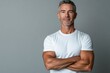 © MUdaylah - Happy confident handsome fit sporty healthy mature older man, middle aged sportsman athlete or personal trainer wearing white t-shirt standing isolated on gray with generative ai