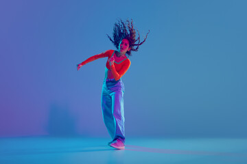 Canvas Print - Hip hop training session in full motion, female dancer performing with passion against gradient blue background in neon light. Concept of freestyle dance, modernity, urban culture, youth