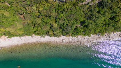 coastline from above, showing greenery with white sand and clear water lighten by the sun