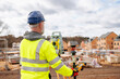 © Iryna - Surveyor in Reflective Gear Using a Total Station on a Construction Site Beneath a Cloudy Sky