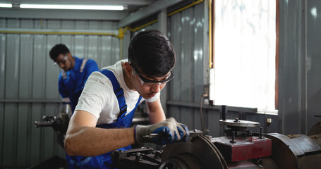 Canvas Print - A man in a blue apron is working on a machine. He is wearing safety glasses and gloves