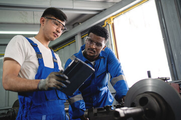 Wall Mural - Two men are working on a machine in a workshop. One of them is wearing a blue shirt and the other is wearing a white shirt