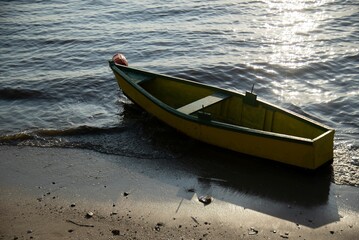 Wall Mural - Yellow wooden boat on shore with sunlight reflecting on water