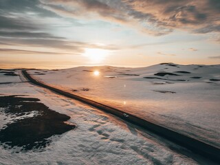 Wall Mural - Car driving through snowy landscape at sunset