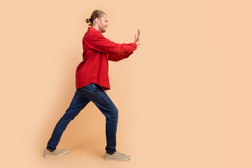 Wall Mural - Full length profile portrait of nice young man arms push empty space wear red shirt isolated on beige color background