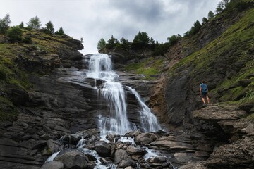 Landscape view of a hiker silhouette standing on a rock in front of a waterfall