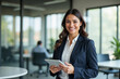 © Pixel Focus AI - Portrait of young Hispanic professional business woman standing in office. Happy female company executive, smiling businesswoman entrepreneur corporate leader manager looking at camera using tablet