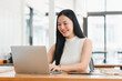 © kenchiro168 - Asian woman working on laptop in bright office, smiling happily