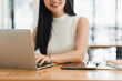 © kenchiro168 - A woman working on laptop, smiling and focused in bright workspace