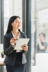 Wall Mural - A confident businesswoman smiles while holding tablet in modern office