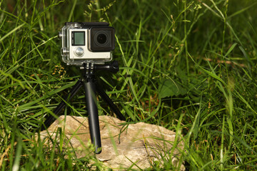 Canvas Print - Modern action camera with tripod in grass outdoors. Space for text