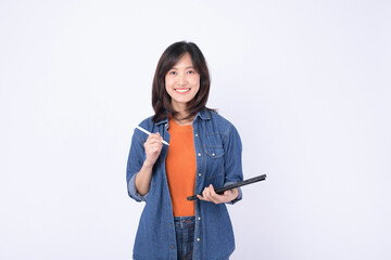 A young woman smiles confidently while holding tablet and pen, dressed in casual denim jacket over an orange top. Her cheerful expression conveys enthusiasm and readiness for work or study