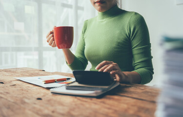 Balancing Act: Woman in Green calculates her finances with a warm beverage in hand. 