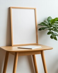 Modern interior scene featuring a wooden table, blank frame, notebook, and lush green plant against a neutral wall.