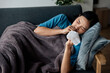 © aksonsat - Woman is ill sick with fever, a runny nose and cough feeling under weather under blanket in the living room at home and wipe a nose with facial tissue.
