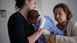 © Marco - Elderly woman and another woman tending to a newborn baby wrapped in a blue blanket, focusing on the infant's comfort and care