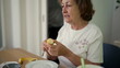 © Marco - Elderly woman peeling a banana at the table, illustrating a simple and peaceful moment of daily life in a cozy home environment