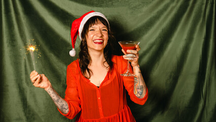 A beautiful happy young woman in a Santa hat holds a cocktail and a sparkler