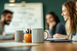 © SejutaCahaya - A white coffee mug sits on a wooden table in front of a group of people in a meeting.