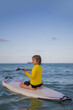 © Volodymyr - Kid riding on a paddle board. Summer holidays. Kid paddle surf surfer little blonde boy in summer beach. Happy Child floating on a paddleboard in the sea.
