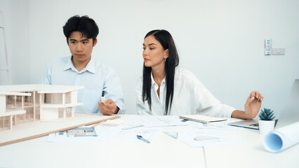 Wall Mural - Professional male engineer measure house model by using ruler while beautiful cooperative coworker working together by using laptop to analysis data. Creative design and teamwork. Closeup. Immaculate.