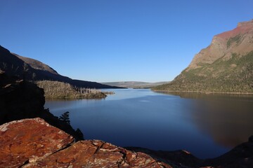 Wall Mural - Serene lake surrounded by mountains under clear blue sky