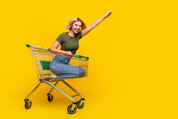 Canvas Print - Full size photo of overjoyed girl dressed khaki crop top ride in shopping cart to empty space fist up isolated on yellow color background