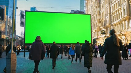 people stroll by a massive green screen in a bustling urban area, enjoying the lively atmosphere of 