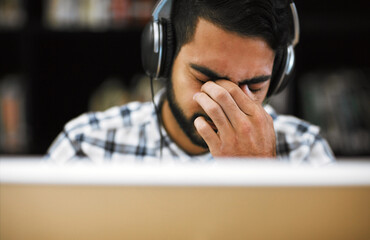 Leinwandbilder - Man, university student and eye strain on computer with headphones in library for internet, online error and research. Male person, tired and burnout or headache with assignment deadline and study