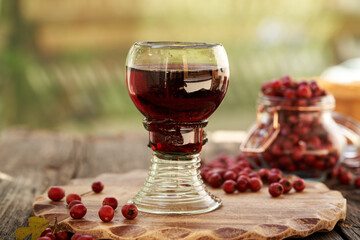 Wall Mural - Medicinal wine made from fresh wild hawthorn berries in a cup made of forest glass full of air bubbles