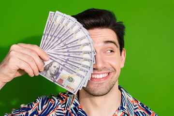 Poster - Photo of cheerful guy with stylish haircut dressed print shirt dollars cover eye look empty space isolated on green color background