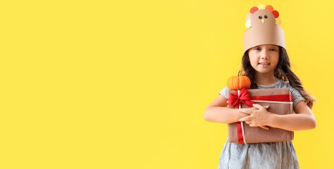 Wall Mural - Cute little girl holding gift and pumpkin on yellow background with space for text. Thanksgiving Day celebration