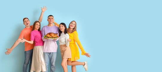 Poster - Happy friends holding tasty baked turkey on light blue background with space for text. Thanksgiving Day celebration