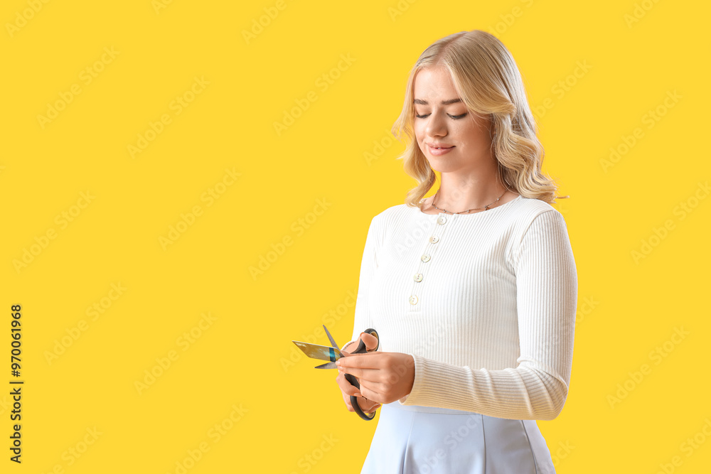 Young woman cutting credit card on yellow background