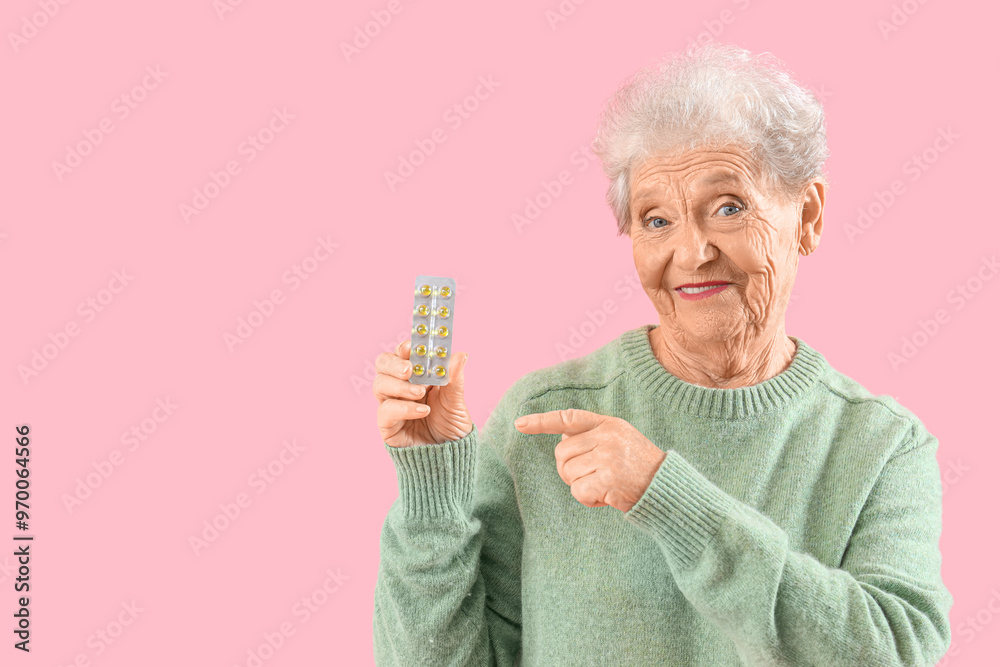 Senior woman pointing at pills on pink background