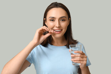 Sticker - Pretty young woman with glass of water taking pill on grey background