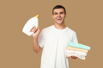 Young man with clean towels and bottle of detergent on beige background