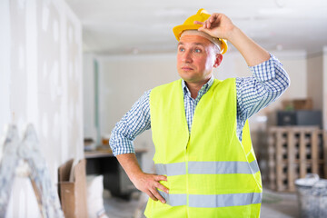 Frustrated worker in yellow vest and hard hat is dissatisfied with the way the walls are plastered