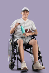 Wall Mural - Sporty young man in wheelchair with rugby ball and water bottle on lilac background