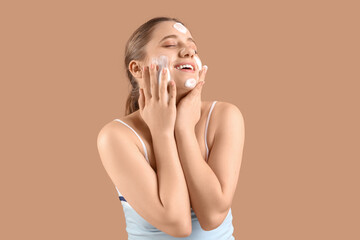 Wall Mural - Beautiful young woman applying cosmetic foam on her face against brown background